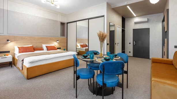 A modern hotel room with a large bed, a dining table with chairs, a sofa, and a mirror. - Jam Apartments (Lviv)
