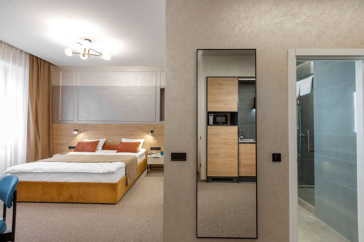 A modern hotel room with a large bed, a bedside table, a built-in wardrobe, and a separate bathroom with a shower.