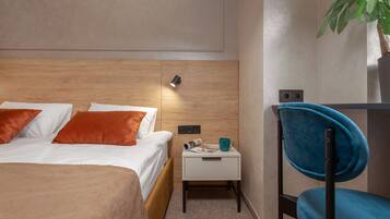 Habitación de hotel ordenada con cama, mesita de noche pequeña, una silla y una lámpara fijada a la pared.