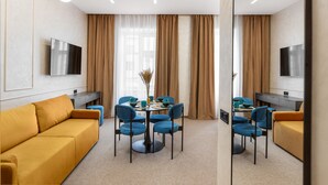 A modern hotel room with a sofa, dining table, chairs, and a TV. - Jam Apartments (Lviv)