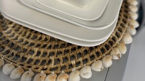Et hvidt porcelænsstel med kop og underkop på en vævet bordskåner med skaller, placeret på et bord.