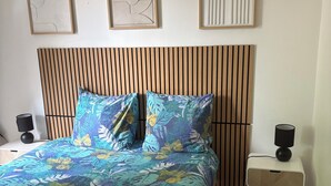 Et soveværelse med seng, sengebord, lampe og billedkunst på væggen.