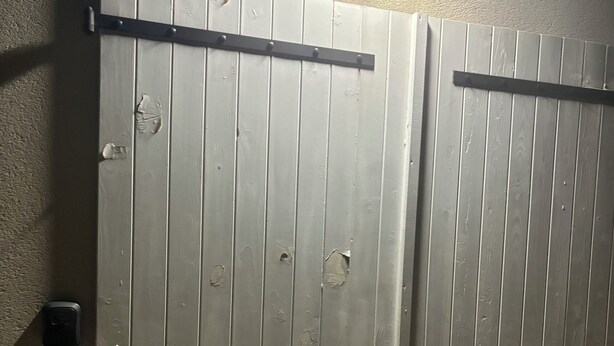 Et sæt dobbelt døre med en vandret stang i midten, en vægmonteret lampe over døren og et dørhåndtag på venstre side.