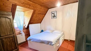 A bedroom with a sloped ceiling, a bed, a radiator, and a window with curtains. - Maison avec piscine proche des plages (Friville-Escarbotin)