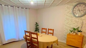 A dining area with a round table, four chairs, a wooden cabinet, and a clock on the wall. - Maison avec piscine proche des plages (Friville-Escarbotin)