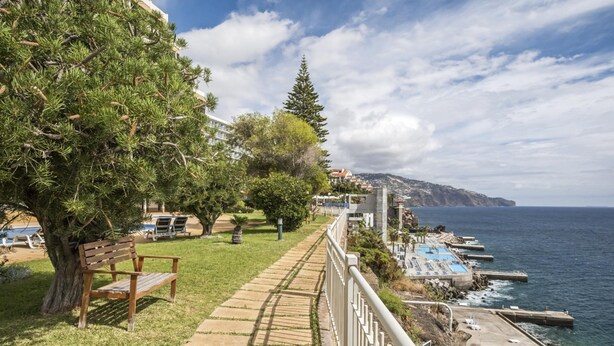 A coastal walkway with a bench, trees, and a view of the sea and buildings. - Central Lido Apartment by Homie (Funchal)