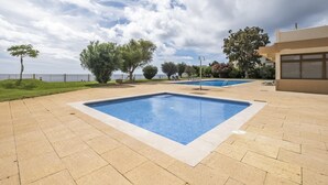 A rectangular outdoor swimming pool with a clear blue water surface, surrounded by a paved area with beige tiles. - Central Lido Apartment by Homie (Funchal)
