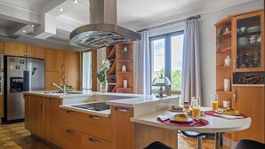 A modern kitchen with wooden cabinets, a stainless steel refrigerator, a built-in oven, and a dining area with a table and chairs. - Central Lido Apartment by Homie (Funchal)
