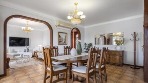 A dining area with a wooden table and chairs, a chandelier, and a television in the background. - Central Lido Apartment by Homie (Funchal)