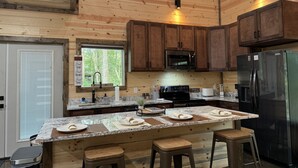 A modern kitchen with wooden cabinetry, a stainless steel refrigerator, a microwave, and a large island with stools. - The Beautiful Moonlight Dream Cabin in Broken Bow is STUNNING! (Broken Bow)