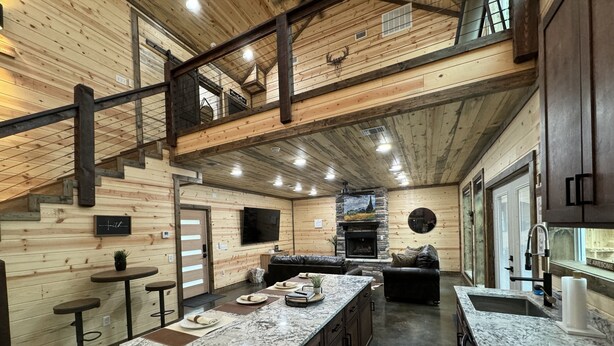 A spacious kitchen with a large island, dark wood cabinets, and a stone fireplace. - The Beautiful Moonlight Dream Cabin in Broken Bow is STUNNING! (Broken Bow)