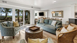 A spacious living area with a large sofa, two armchairs, a dining table, and a TV mounted on the wall.