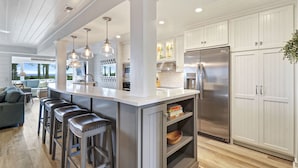 A modern kitchen with a central island, bar stools, a refrigerator, and a view to the outside.