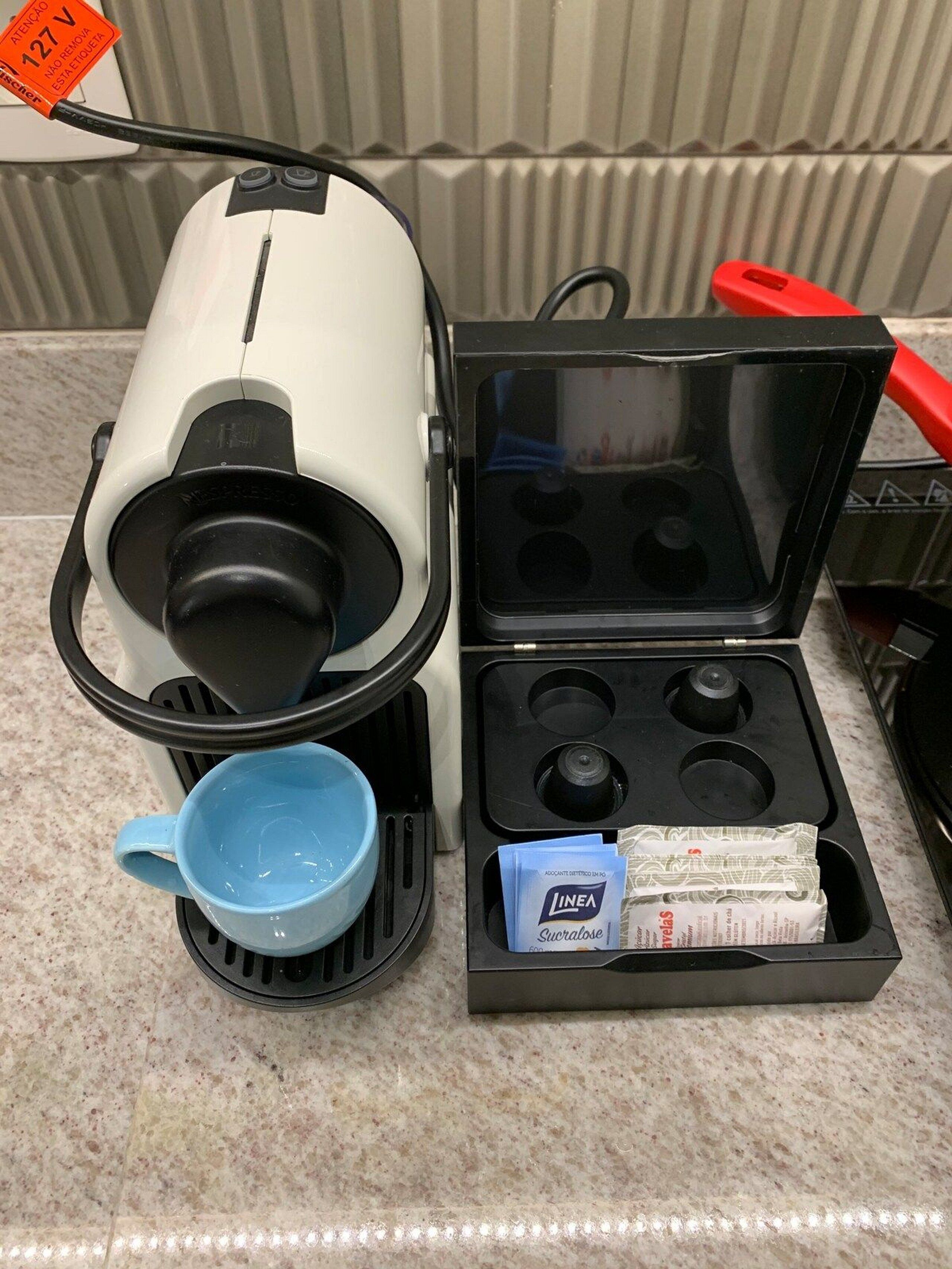 A coffee maker with a cup holder, a packet of coffee pods, and a red object on a countertop.