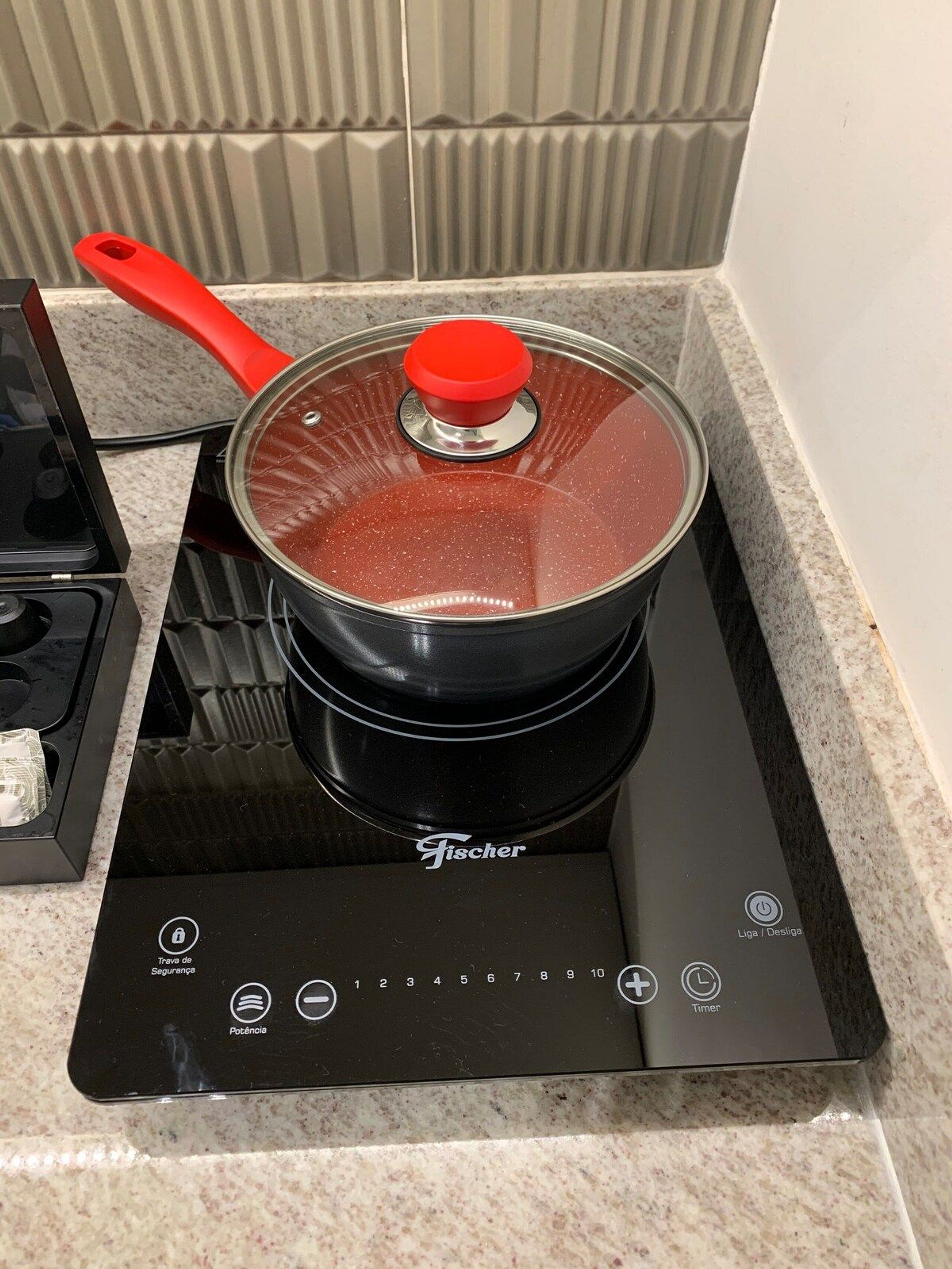 Una cocina con tope de inducción negro y una olla roja encima.