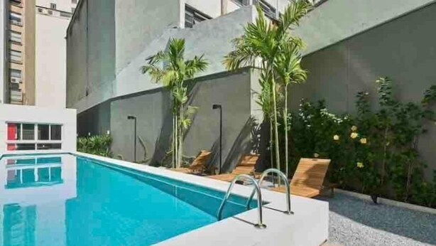A modern pool area with a clear blue pool, surrounded by palm trees and a concrete wall. - Luz 1109 (São Paulo)