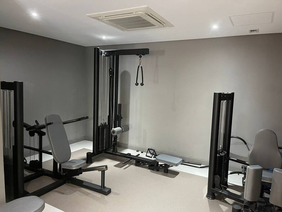 Uma academia com diversos equipamentos de exercício, incluindo um banco de musculação, suporte para agachamento e aparelho de polia.