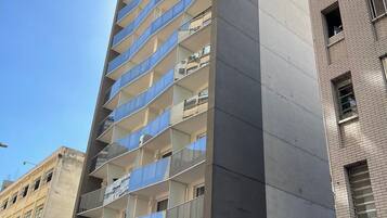 Un edificio alto con varios balcones, una tienda con letreros y un cielo azul despejado.