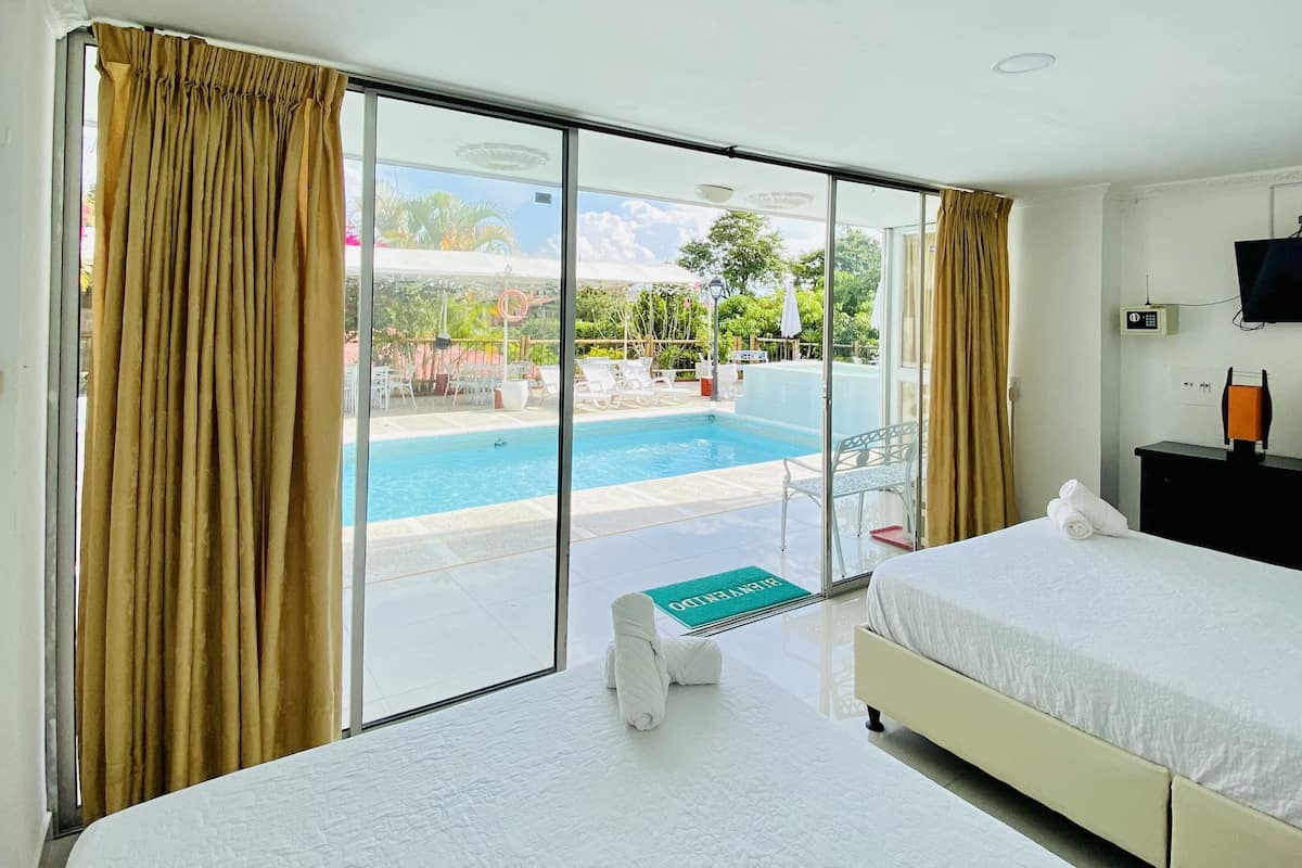 A hotel room with two beds, a large window with curtains, a pool view, and a bedside table with a towel.