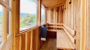 Une cabane en bois avec un banc et une petite table, de grandes fenêtres et une vue sur la verdure.