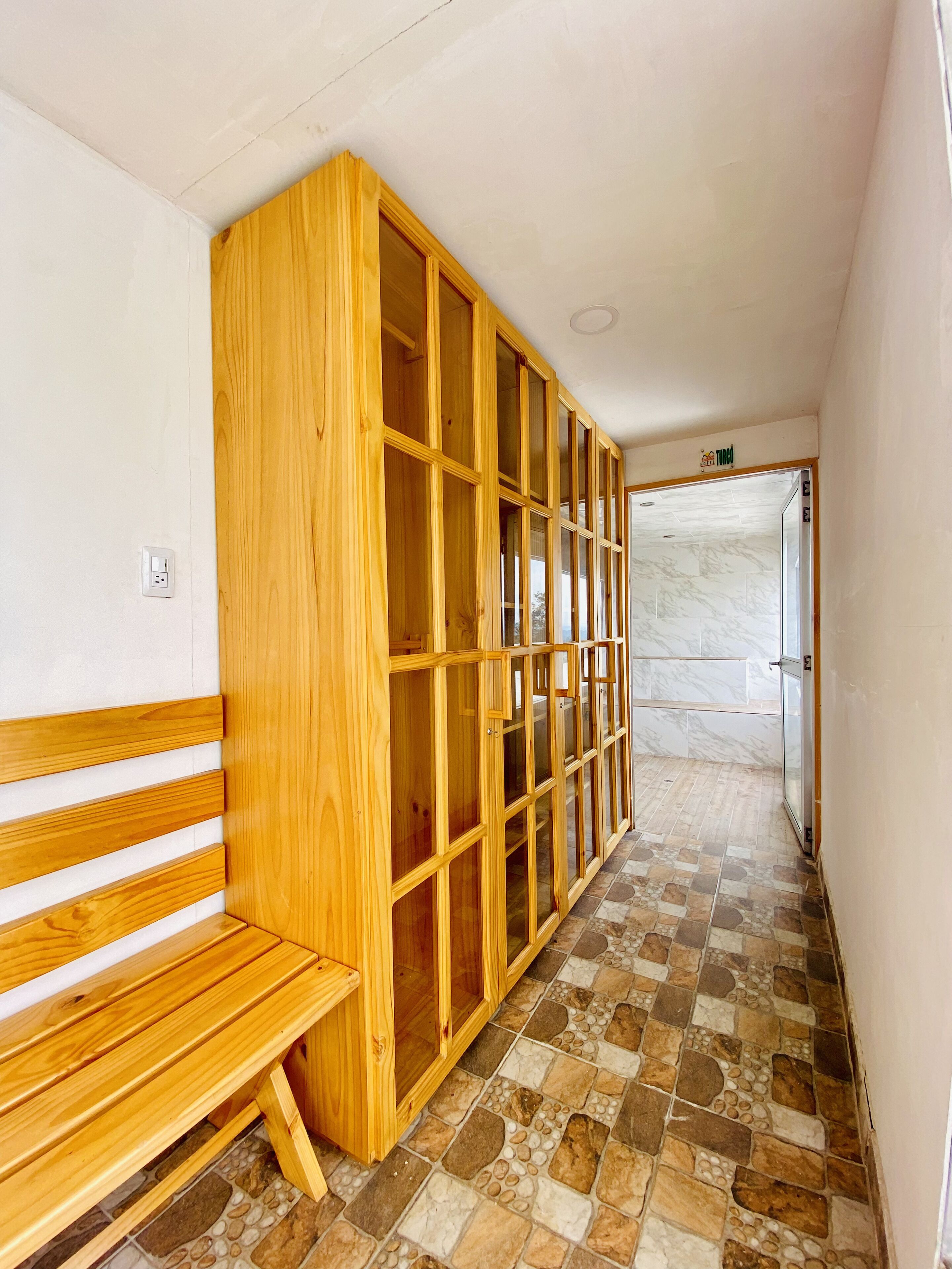 A hallway with a wooden bench, a large wooden cabinet with glass doors, and a tiled floor.