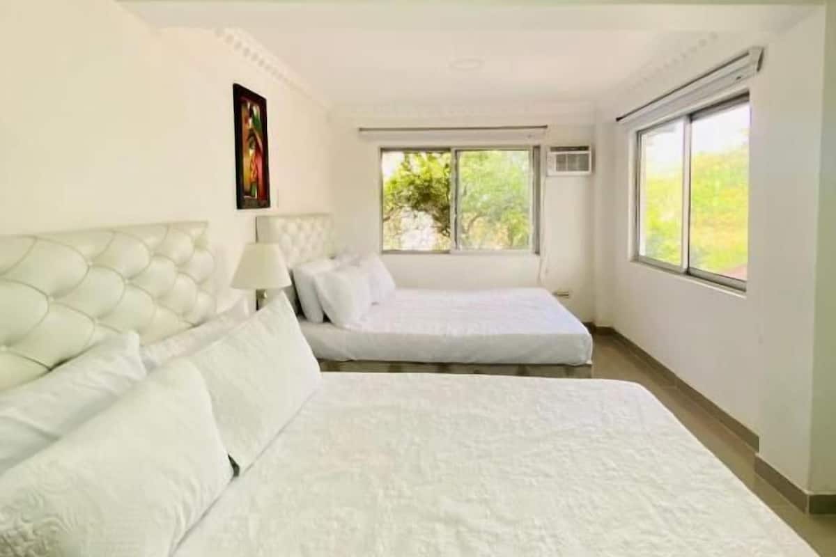 A bedroom with two beds, a window, and a ceiling light.