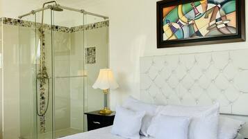 Una habitación de hotel con una cama grande, ducha con paredes de vidrio, un cuadro en la pared y un cabecero acolchado.