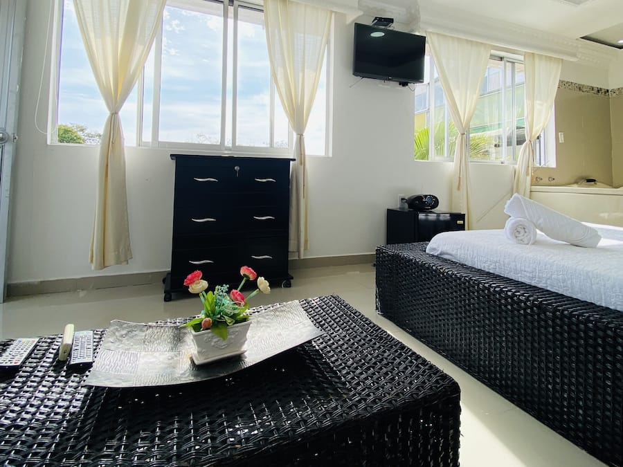 Una habitación de hotel con cama, cómoda, televisor y ventana con cortinas.
