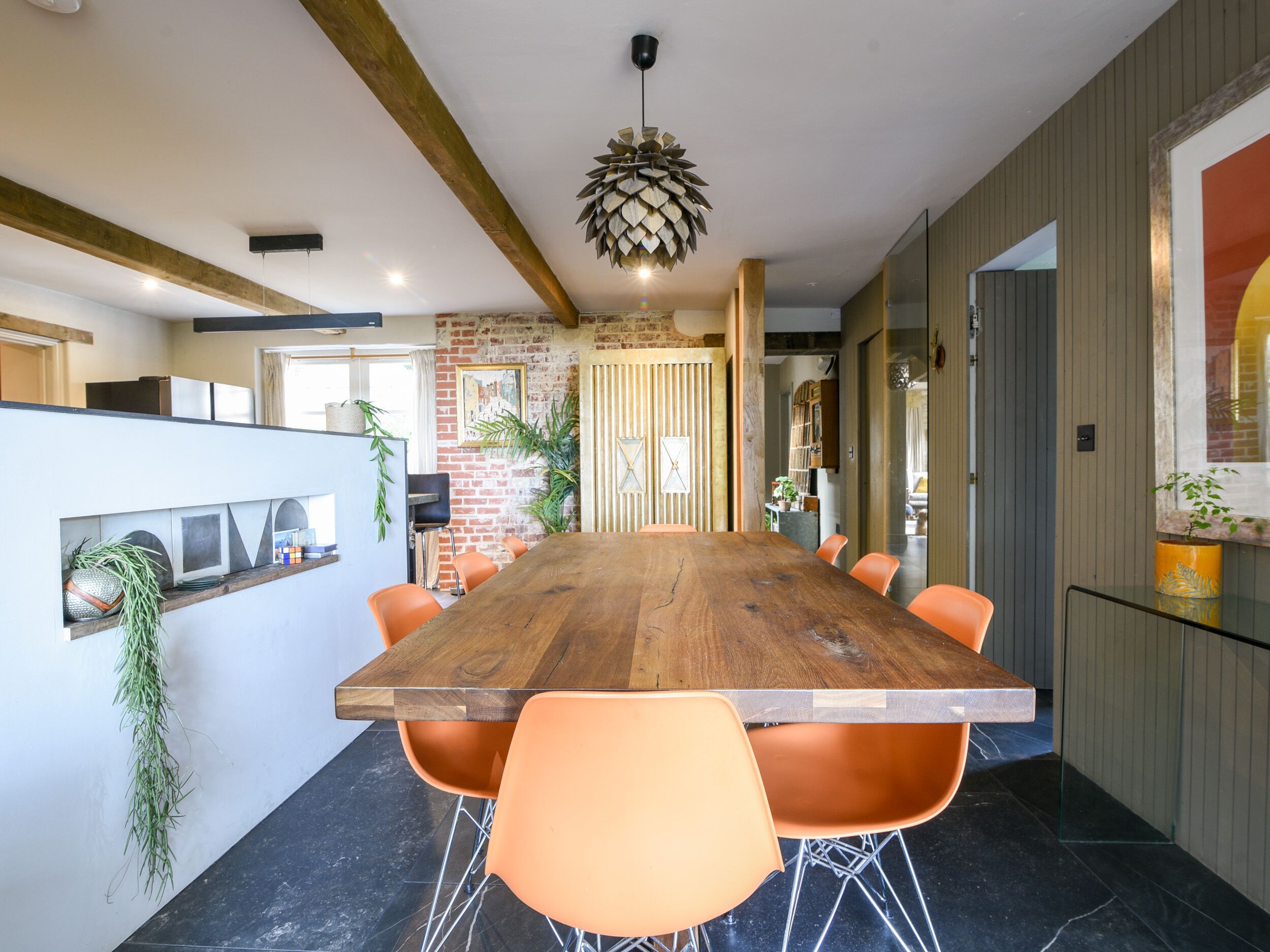 A modern dining area with a large wooden table, orange chairs, and a unique ceiling light.