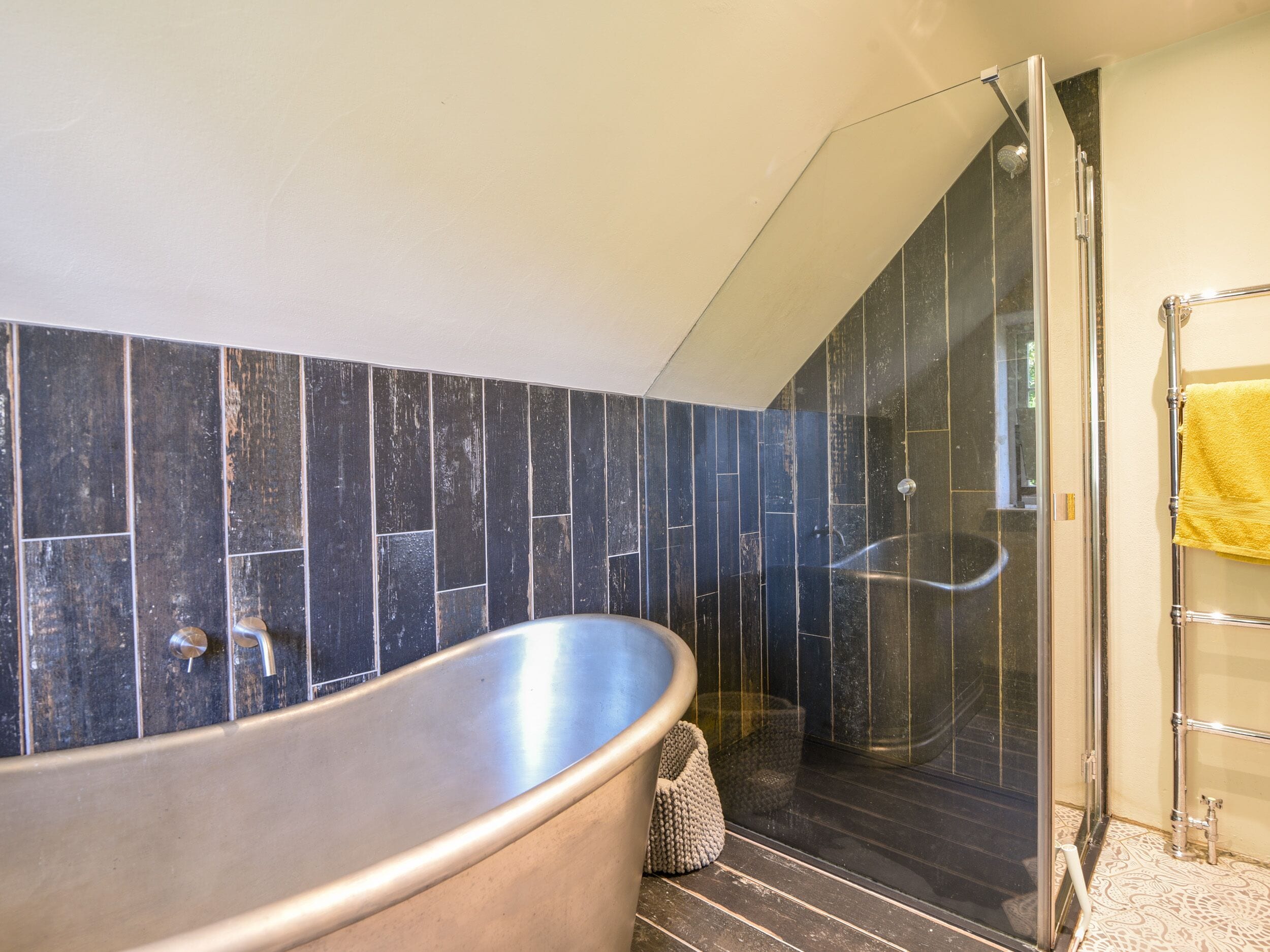Une salle de bain avec une baignoire sur pieds, une douche à parois de verre et une serviette jaune posée sur un porte-serviettes.