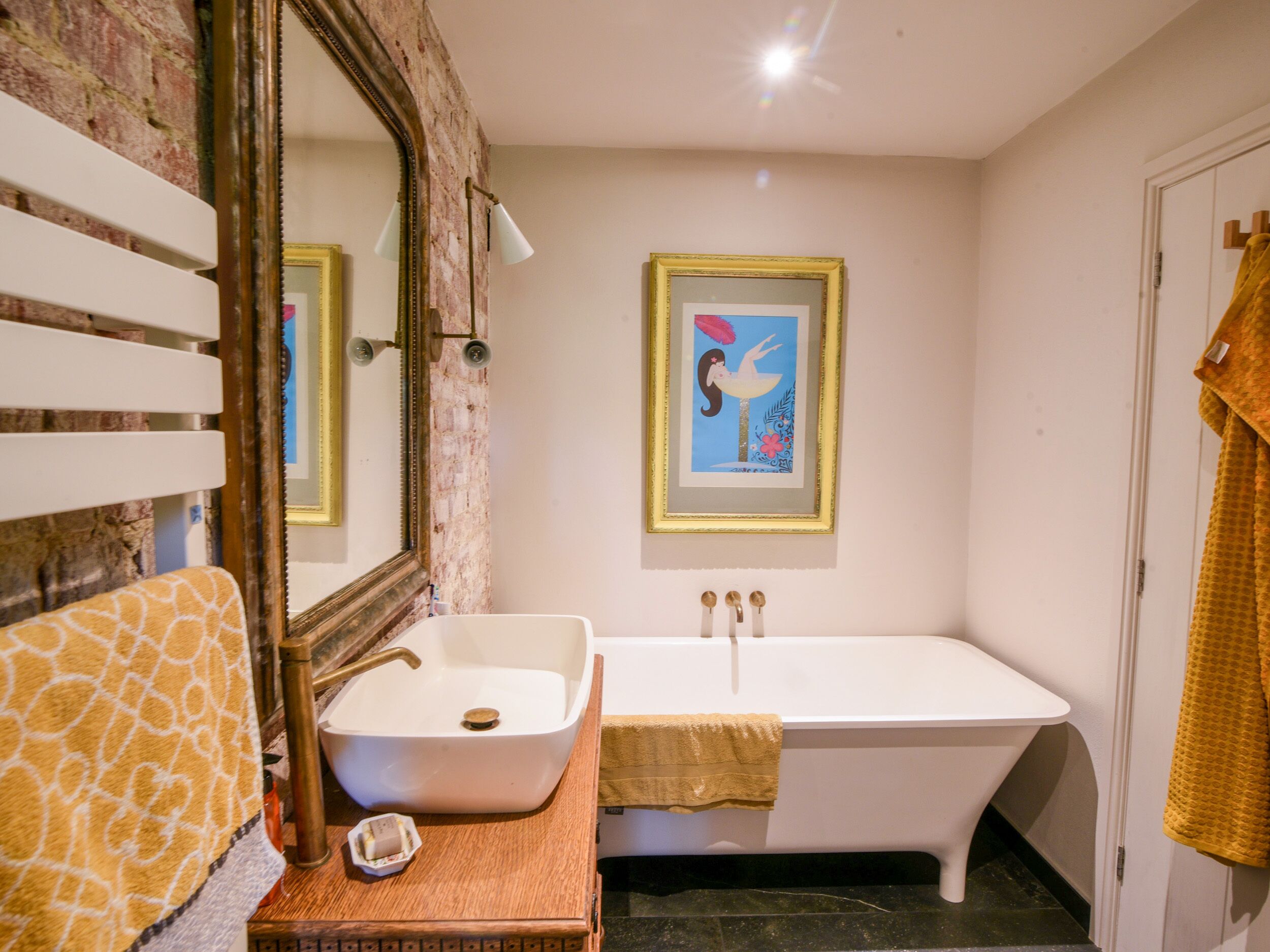 Un baño con un lavabo blanco, una bañera, un espejo grande y un cuadro enmarcado en la pared.