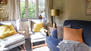 A cozy living room with stone walls, a blue sofa, two armchairs, and a lamp. - The Carriage House (Lyme Regis)