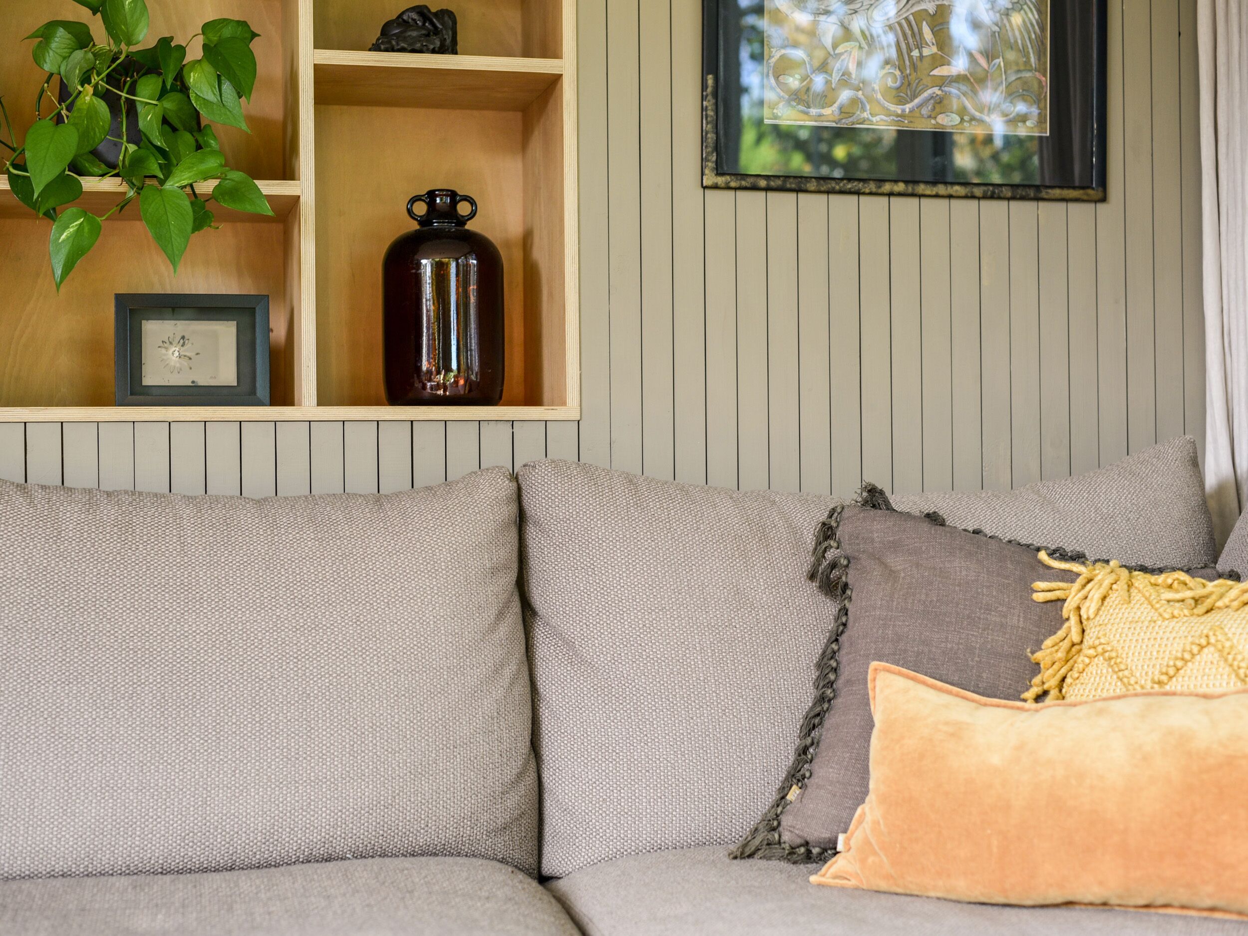 A grey sofa with a yellow throw pillow and a decorative glass vase on a wooden shelf.