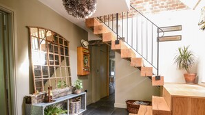 A staircase with wooden steps and metal railings, leading to a room with a large mirror, a cabinet, and a potted plant. - The Carriage House (Lyme Regis)