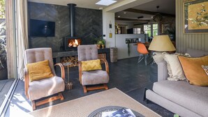 A modern living room with a fireplace, comfortable seating, and a kitchen area in the background. - The Carriage House (Lyme Regis)