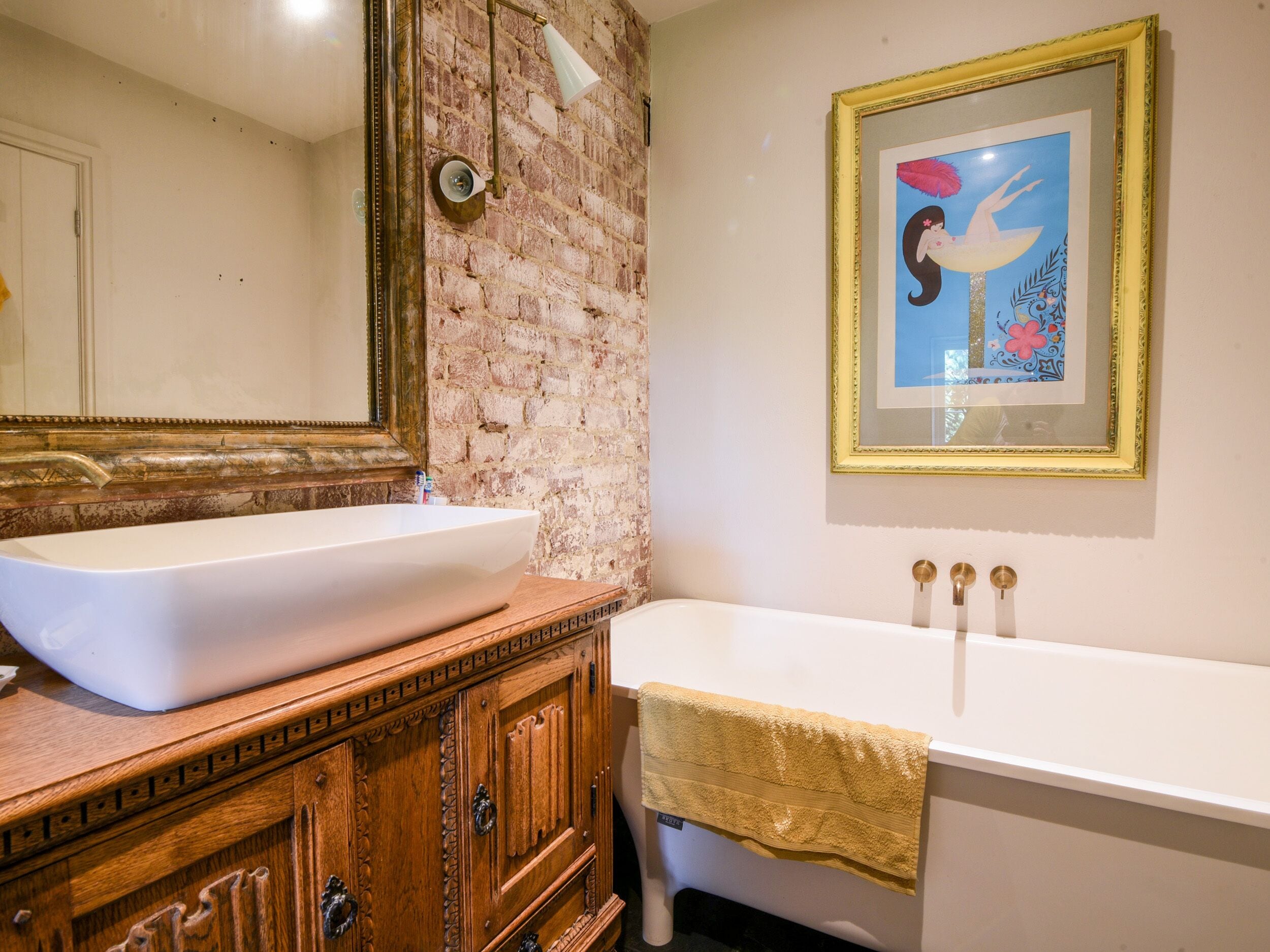 A bathroom with a large white sink, a wooden vanity, a white bathtub, and a framed picture on the wall.