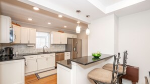 A modern kitchen with white cabinetry, a black countertop, and a built-in island with bar stools. - Cozy and Close to Kings Island (Kings Mills)