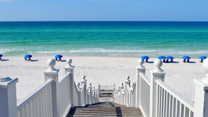 A wooden staircase leading to a beach with white railings and blue umbrellas.