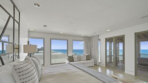 A spacious bedroom with a large bed, a sitting area with a sofa, and a balcony with a view of the ocean.