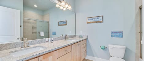 Un baño con un espejo grande, encimera de granito, armarios de madera y un inodoro blanco.