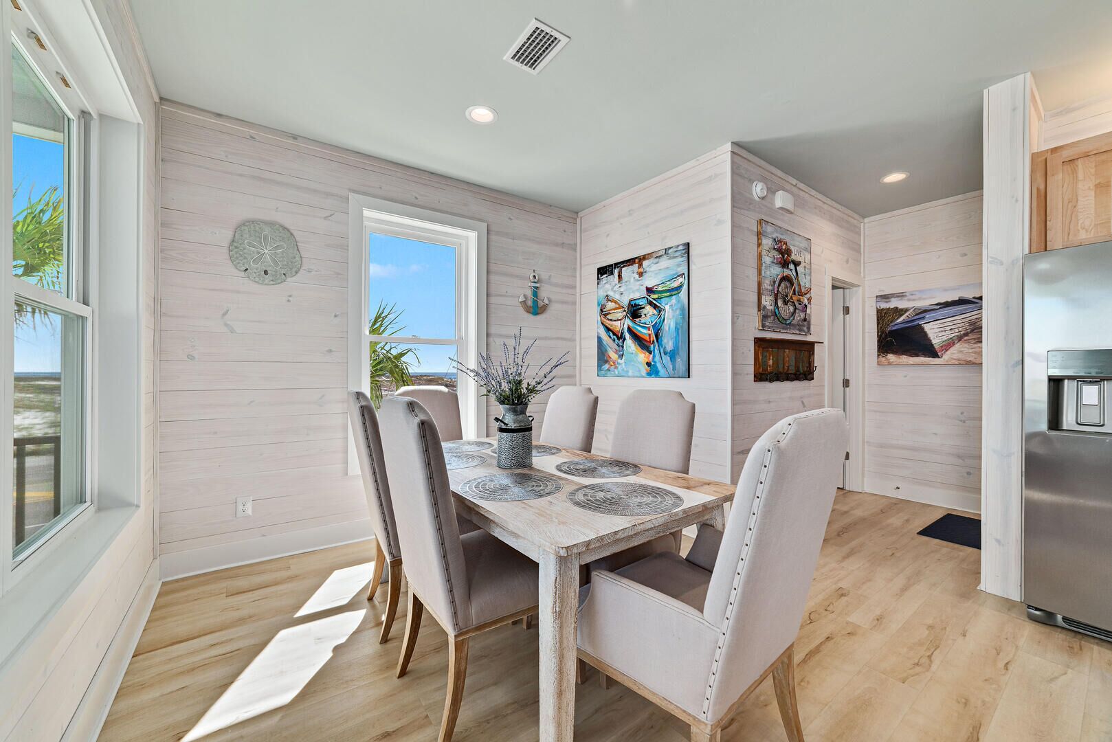 A modern kitchen with a wooden table, white chairs, and a stainless steel refrigerator.