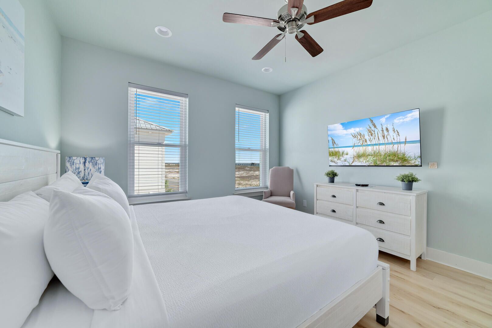 A bedroom with a bed, a ceiling fan, a TV, and a window with blinds.