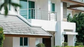 Stylish two-story residence with a flat roof and balcony, surrounded by lush greenery and a well-manicured entrance.