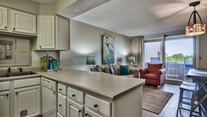 A modern kitchen with white cabinets, a central island, and a dining area with a red chair and a laptop. - Jetty View at Jetty East! One FREE Beach Chair Setup Each Day of Your Stay! (Destin)