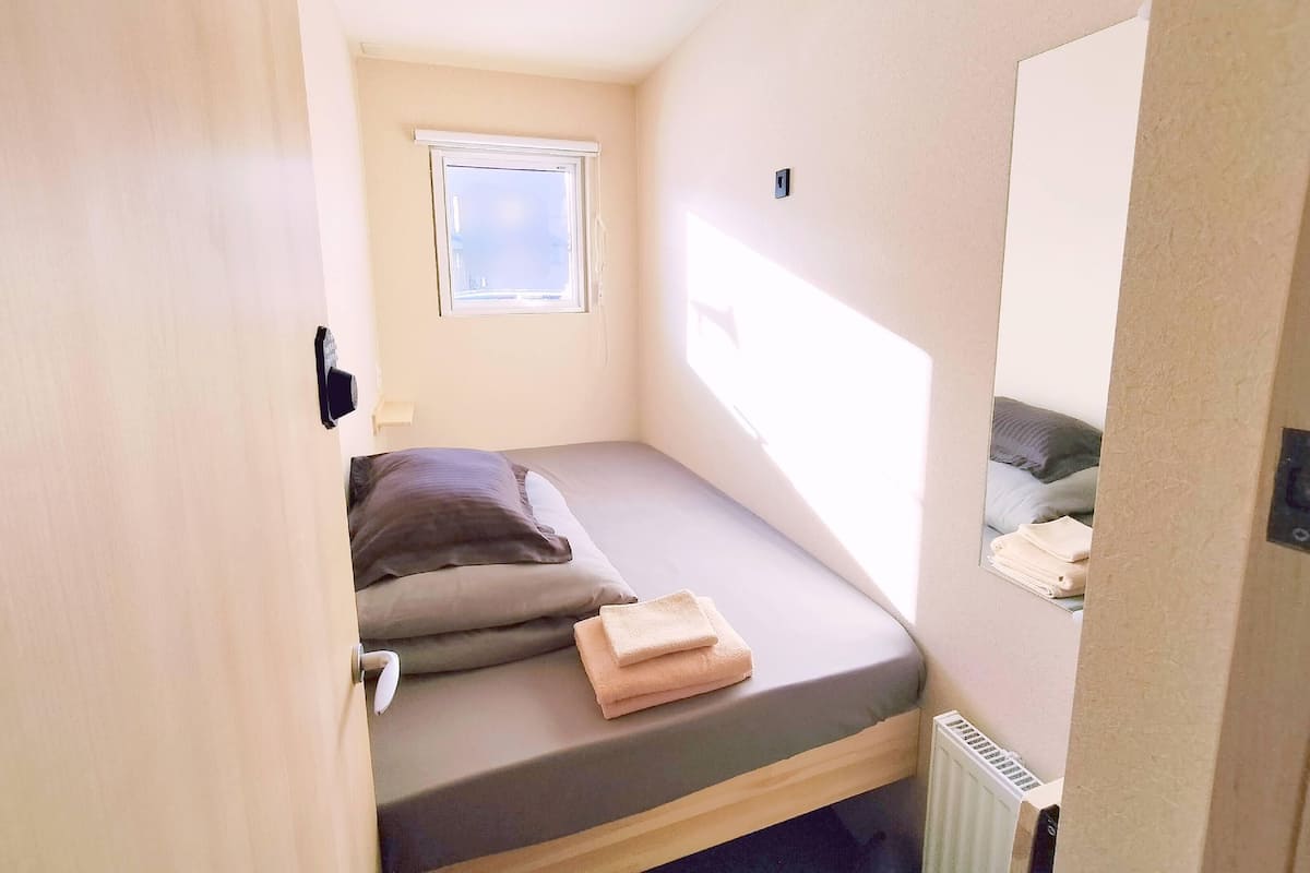 Une petite chambre avec un lit simple, une petite fenêtre et un radiateur.