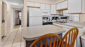 A modern kitchen with white cabinets, a central island with chairs, a microwave, and a dishwasher. - Sunrise gulf view/beach front condo! Enjoy one free beach chair set up each day (Destin)
