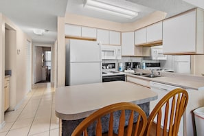 Una cocina moderna con armarios blancos, una isla central con sillas, un microondas y un lavavajillas.