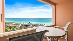 A balcony with a table and chairs, overlooking a beach with a pier and umbrellas. - Sunrise gulf view/beach front condo! Enjoy one free beach chair set up each day (Destin)