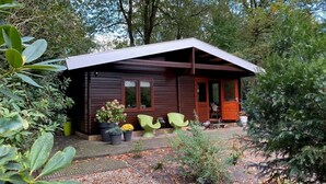 Una cabaña de madera con techo inclinado, rodeada de árboles y plantas en macetas.