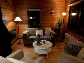 Een gezellig interieur van een chalet met een bank, fauteuils, een kleine ronde tafel, een lamp en een opgehangen hertenkop.